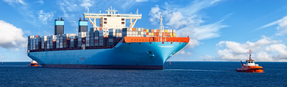 A full loaded container ship being towed by tugs on a flat calm sea